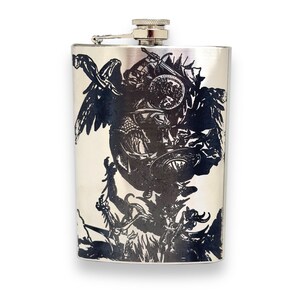 May include: A silver flask featuring a black and white graphic design of a winged creature wielding a sword and shield. The design is intricate and detailed.