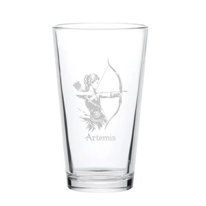 May include: Clear pint glass featuring an etched design of Artemis, the Greek goddess of the hunt, with a bow and arrow. The word "Artemis" is etched below the image. The glass is suitable for beverages.
