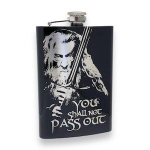 May include: Black stainless steel flask with a silver image of Gandalf from The Lord of the Rings holding a sword. The text "You Shall Not Pass Out" is printed below the image.
