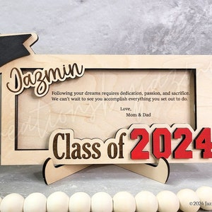 May include: A wooden graduation frame with the name "Dazmin" and "Class of 2024" in a decorative font. The frame includes a graduation cap and a message from Mom & Dad. The frame is designed to hold a photo.