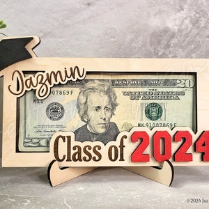 May include: A wooden graduation money holder with a $20 bill visible. The frame features the name "Jazmin", the words "Class of 2024", and a graduation cap. The numbers "2024" are in red.