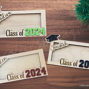 May include: Wooden graduation frames with the names "Yadira", "Caden", and "Jonikah" and the text "Class of 2024". Each frame has a graduation cap design. The frames are made of light-colored wood and are displayed on a wooden surface.