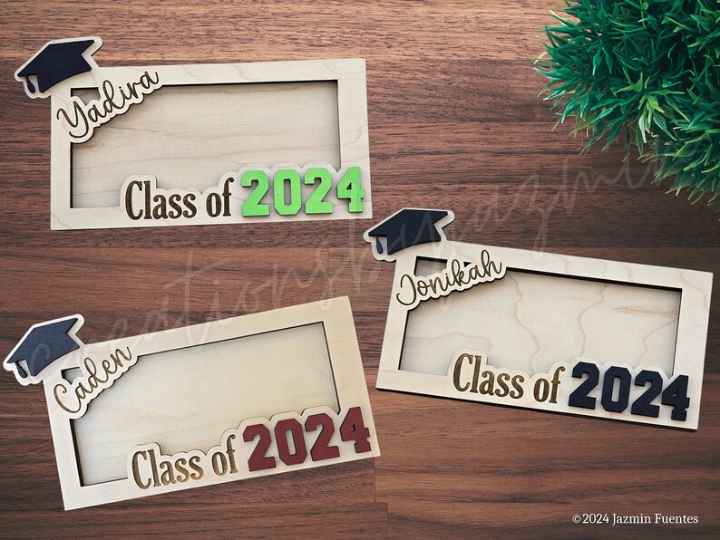 May include: Wooden graduation frames with the names "Yadira", "Caden", and "Jonikah" and the text "Class of 2024". Each frame has a graduation cap design. The frames are made of light-colored wood and are displayed on a wooden surface.