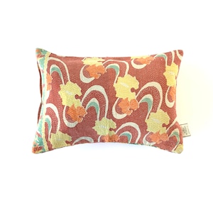 May include: A rectangular pillow with a red background and a floral pattern in shades of yellow, orange, and green. The pillow has a label on the bottom right corner that says "MADE IN INDIA".