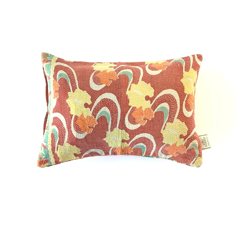 May include: A rectangular pillow with a red background and a floral pattern in shades of yellow, orange, and green. The pillow has a label on the bottom right corner that says "MADE IN INDIA".