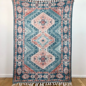 May include: A blue and pink patterned rug with a fringed border. The rug features a geometric design with intricate details.