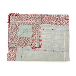 May include: A grey and red woven cotton throw blanket with a fringed edge. The blanket has a geometric pattern in red and a subtle blue pattern.