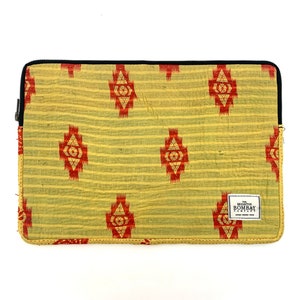 May include: A yellow laptop sleeve with a red and gold geometric pattern. The sleeve has a black zipper and a small rectangular label that reads "The Brighton Bombay Co."