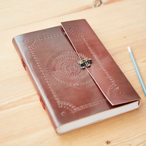 Op de afbeelding: Een bruin lederen dagboek met een decoratief reliëf en een metalen sluiting. Het dagboek is gesloten en ligt op een houten oppervlak.