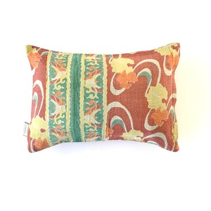 May include: A rectangular pillow with a red, green, and yellow floral pattern. The pillow is made of a soft, quilted fabric.