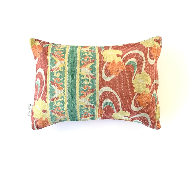 May include: A rectangular pillow with a red, green, and yellow floral pattern. The pillow is made of a soft, quilted fabric.