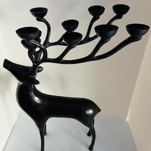 May include: A black metal deer-shaped candelabra. The deer has a sleek, modern design with a smooth, glossy finish. The antlers extend outwards, holding eight candle holders. The candelabra is a decorative piece for home decor.
