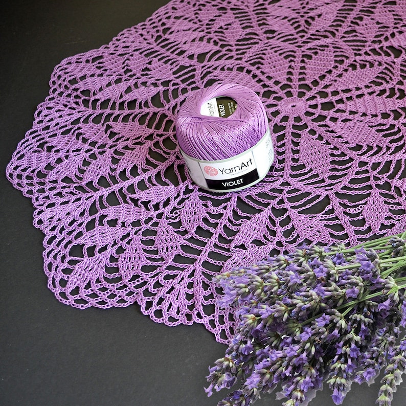 Puede incluir: Un encaje de ganchillo morado con un ovillo de hilo morado y un ramo de flores de lavanda.