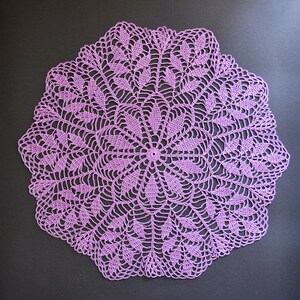 Puede incluir: Un delicado encaje de ganchillo de color morado con un dise&ntilde;o circular que presenta intrincados patrones florales.