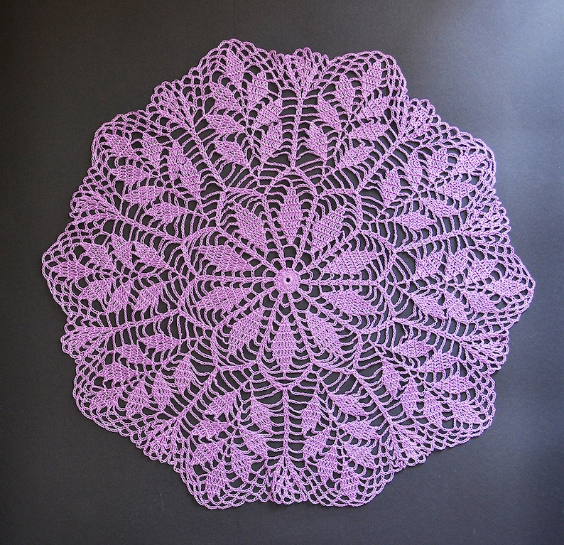 Puede incluir: Un delicado encaje de ganchillo de color morado con un dise&ntilde;o circular que presenta intrincados patrones florales.