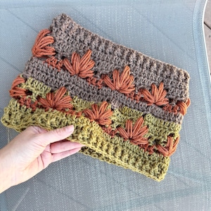 May include: A crocheted cowl with a brown, green, and orange color scheme. The cowl features a repeating pattern of crocheted leaves.