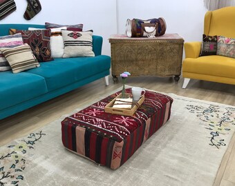 Può includere: Un divano blu turchese con una varietà di cuscini decorativi con motivi, una poltrona gialla con un cuscino con motivi, uno scrigno in legno con dettagli intagliati e un pouf con motivi rossi e neri con un vassoio in legno sopra. La stanza è decorata in stile bohémien con un tappeto con motivi sul pavimento.