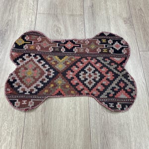 Handmade colorful Turkish Kilim pet mats, boho upcycled rug designed for pets, unique bone-shaped feeding mat, durable woven fabric, eco-friendly recycled carpet, decorative home accent, vibrant patterns and textures, comfortable and easy-to-clean, perfect for indoor or outdoor use, adds charm to any pet feeding area, ideal gift for pet lovers, artisanal inspired Turkish weave, stylish addition to pet space, one-of-a-kind handmade design.