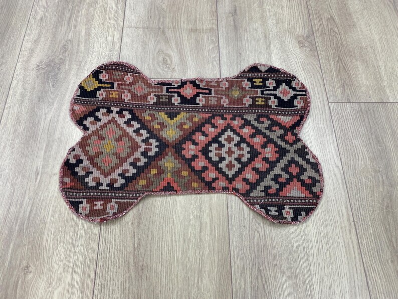 Handmade colorful Turkish Kilim pet mats, boho upcycled rug designed for pets, unique bone-shaped feeding mat, durable woven fabric, eco-friendly recycled carpet, decorative home accent, vibrant patterns and textures, comfortable and easy-to-clean, perfect for indoor or outdoor use, adds charm to any pet feeding area, ideal gift for pet lovers, artisanal inspired Turkish weave, stylish addition to pet space, one-of-a-kind handmade design.