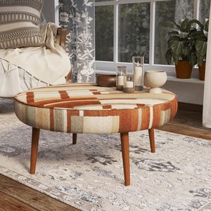 May include: A round ottoman featuring a geometric pattern in shades of rust orange, beige, and grey. The piece is supported by four tapered wooden legs and has a low-profile design with a cushioned top surface suitable for use as a footrest.
