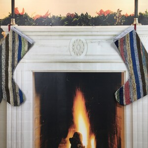 May include: Two colorful striped Christmas stockings hang above a fireplace with a roaring fire. The stockings are made from repurposed fabric and have a rustic, handmade look.