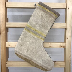 Puede incluir: Una media de color crema con rayas amarillas y beige cuelga de una escalera de madera. La media está hecha de un tejido tejido y tiene un aspecto rústico y vintage.