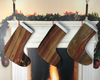 Puede incluir: Tres calcetines de Navidad a rayas marrones y beige con ribete blanco colgados de una repisa de chimenea blanca sobre una chimenea.