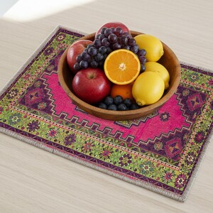 A wooden bowl filled with various fruits, including apples, oranges, and grapes, sits on a colorful, patterned placemat on a wooden table.