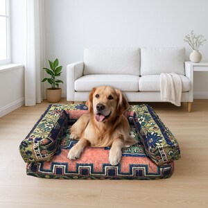 May include: A dog bed with a patterned design, featuring a golden retriever. The bed has armrests and a colourful, intricate pattern with red, blue, and green hues. The dog is relaxed, with its tongue out, in a well-lit room.