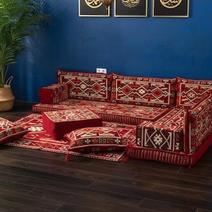 May include: A floor seating set featuring a deep red base color with intricate geometric patterns in white, black, and gold. The set includes a long rectangular floor cushion, backrest cushions, armrest blocks, a square ottoman, and two throw pillows.