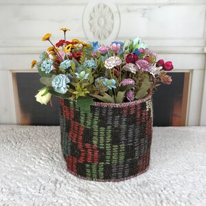 Puede incluir: Una cesta tejida con un patrón geométrico colorido contiene un ramo de flores artificiales. Las flores son una mezcla de rosa, azul, amarillo y blanco.
