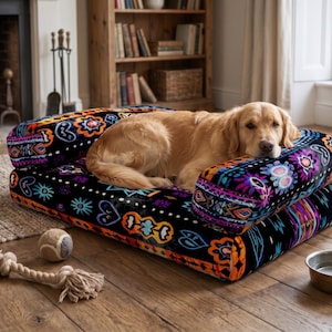 May include: A rectangular pet bed with a black base featuring a vibrant, multicolored geometric and floral pattern. The bed has raised, cushioned sides and a soft surface. A golden-colored dog is resting on the bed, with a tennis ball and rope toy nearby.