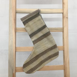 Puede incluir: Una media rayada hecha de tejido tejido en tonos beige y marrón, colgada de una escalera de madera.