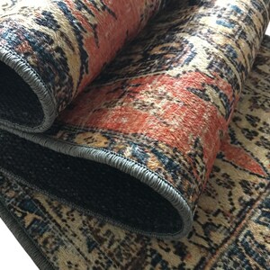 a close-up view of a colorful, patterned rug with a mix of orange, black, and beige colors. The rug has a textured surface and appears to be made of wool or a similar material.