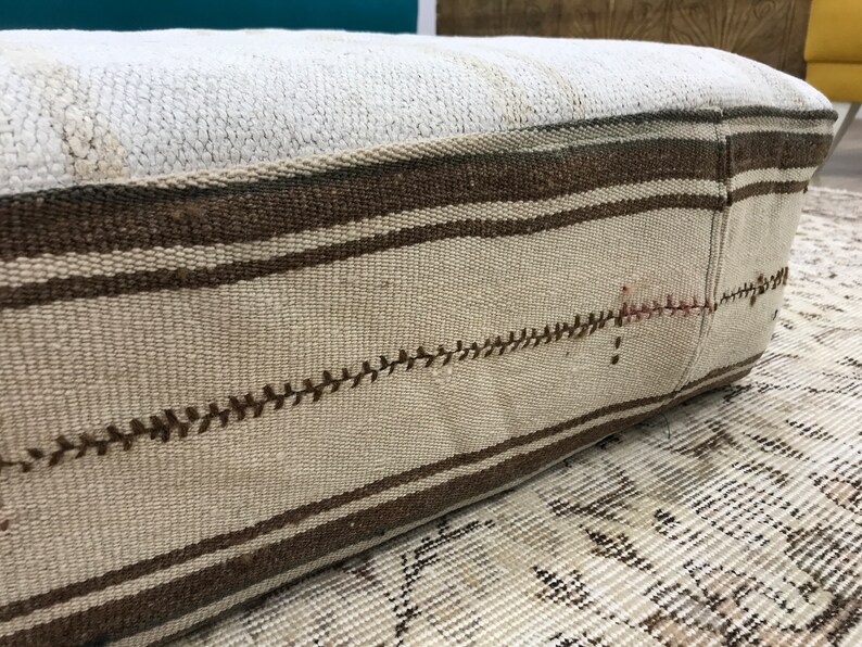 May include: A white and brown striped floor cushion with a stitched design. The cushion is made of woven fabric and has a rectangular shape.