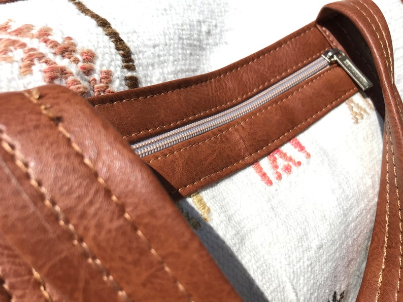 Puede incluir: Primer plano de un bolso de cuero marr&oacute;n con cremallera. El bolso tiene un forro de tela blanca con un patr&oacute;n rosa y marr&oacute;n.