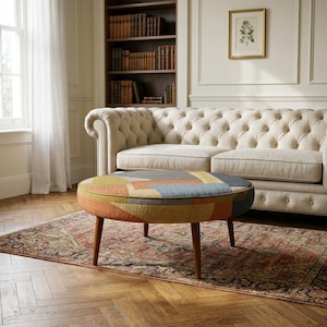 May include: A round ottoman featuring a textured fabric upholstery with a geometric pattern in shades of mustard yellow, burnt orange, slate blue, and gray. The piece is supported by four tapered wooden legs in a medium brown finish.