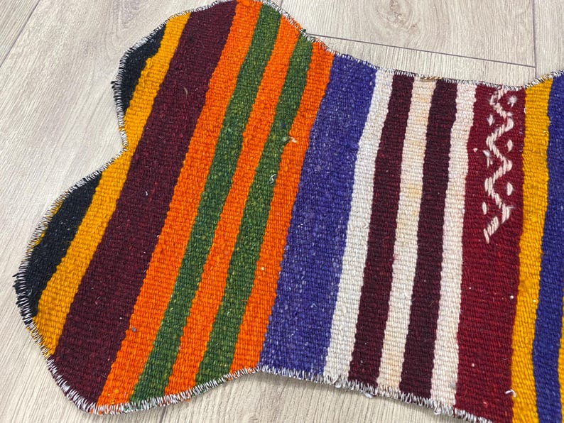 Handmade colorful Turkish Kilim pet mats, boho upcycled rug designed for pets, unique bone-shaped feeding mat, durable woven fabric, eco-friendly recycled carpet, decorative home accent, vibrant patterns and textures, comfortable and easy-to-clean, perfect for indoor or outdoor use, adds charm to any pet feeding area, ideal gift for pet lovers, artisanal inspired Turkish weave, stylish addition to pet space, one-of-a-kind handmade design.