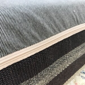 May include: Close-up of a gray and white striped cushion with a zipper closure. The zipper is beige and the fabric is woven.