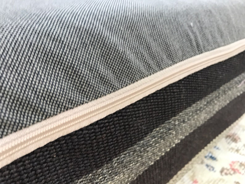 May include: Close-up of a gray and white striped cushion with a zipper closure. The zipper is beige and the fabric is woven.
