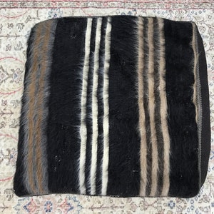 May include: A black and white striped throw pillow with brown accents. The pillow is made of a soft, fuzzy material.