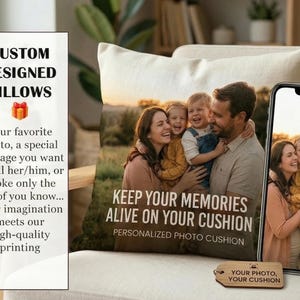 Op de afbeelding: Een gepersonaliseerd fotokussen met een familiefoto, geplaatst op een crèmekleurige stoel. Het kussen heeft de tekst "KEEP YOUR MEMORIES ALIVE ON YOUR CUSHION". Een telefoon toont dezelfde foto. Een label leest "YOUR PHOTO YOUR CUSHION".