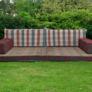 May include: A traditional style sofa with a striped fabric back and floral patterned cushions. The sofa is made of a woven fabric and has a dark gray base.