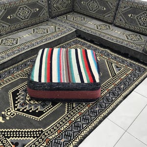 May include: A gray and black patterned rug with a striped cushion in the center. The rug has a geometric design and the cushion has a colorful striped pattern.