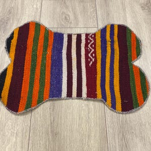 Handmade colorful Turkish Kilim pet mats, boho upcycled rug designed for pets, unique bone-shaped feeding mat, durable woven fabric, eco-friendly recycled carpet, decorative home accent, vibrant patterns and textures, comfortable and easy-to-clean, perfect for indoor or outdoor use, adds charm to any pet feeding area, ideal gift for pet lovers, artisanal inspired Turkish weave, stylish addition to pet space, one-of-a-kind handmade design.