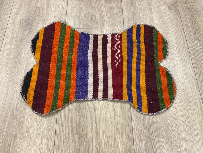 Handmade colorful Turkish Kilim pet mats, boho upcycled rug designed for pets, unique bone-shaped feeding mat, durable woven fabric, eco-friendly recycled carpet, decorative home accent, vibrant patterns and textures, comfortable and easy-to-clean, perfect for indoor or outdoor use, adds charm to any pet feeding area, ideal gift for pet lovers, artisanal inspired Turkish weave, stylish addition to pet space, one-of-a-kind handmade design.