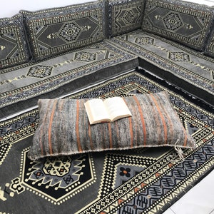 May include: A gray and black patterned floor cushion with a book on top. The cushion is on a gray and black patterned rug.