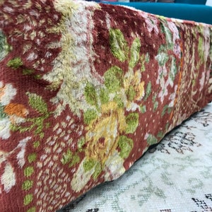 Pode incluir: Um otomano com padr&atilde;o floral vermelho, verde e amarelo com textura felpuda.