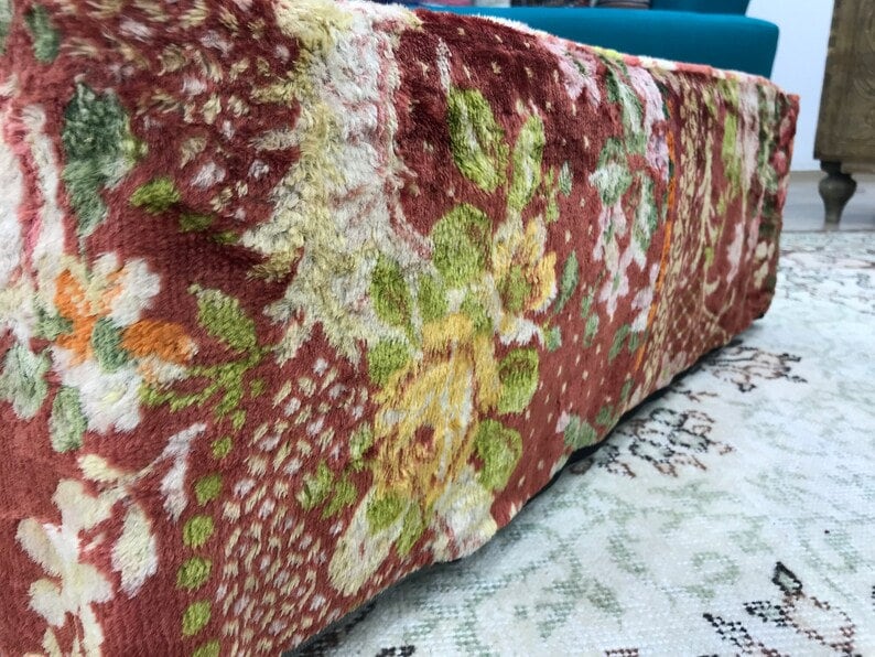 Pode incluir: Um otomano com padr&atilde;o floral vermelho, verde e amarelo com textura felpuda.