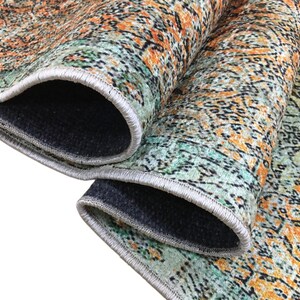 a close-up view of a colorful, patterned rug with a mix of orange, green, and black colors. The rug appears to be folded or rolled up, revealing its intricate design and texture.